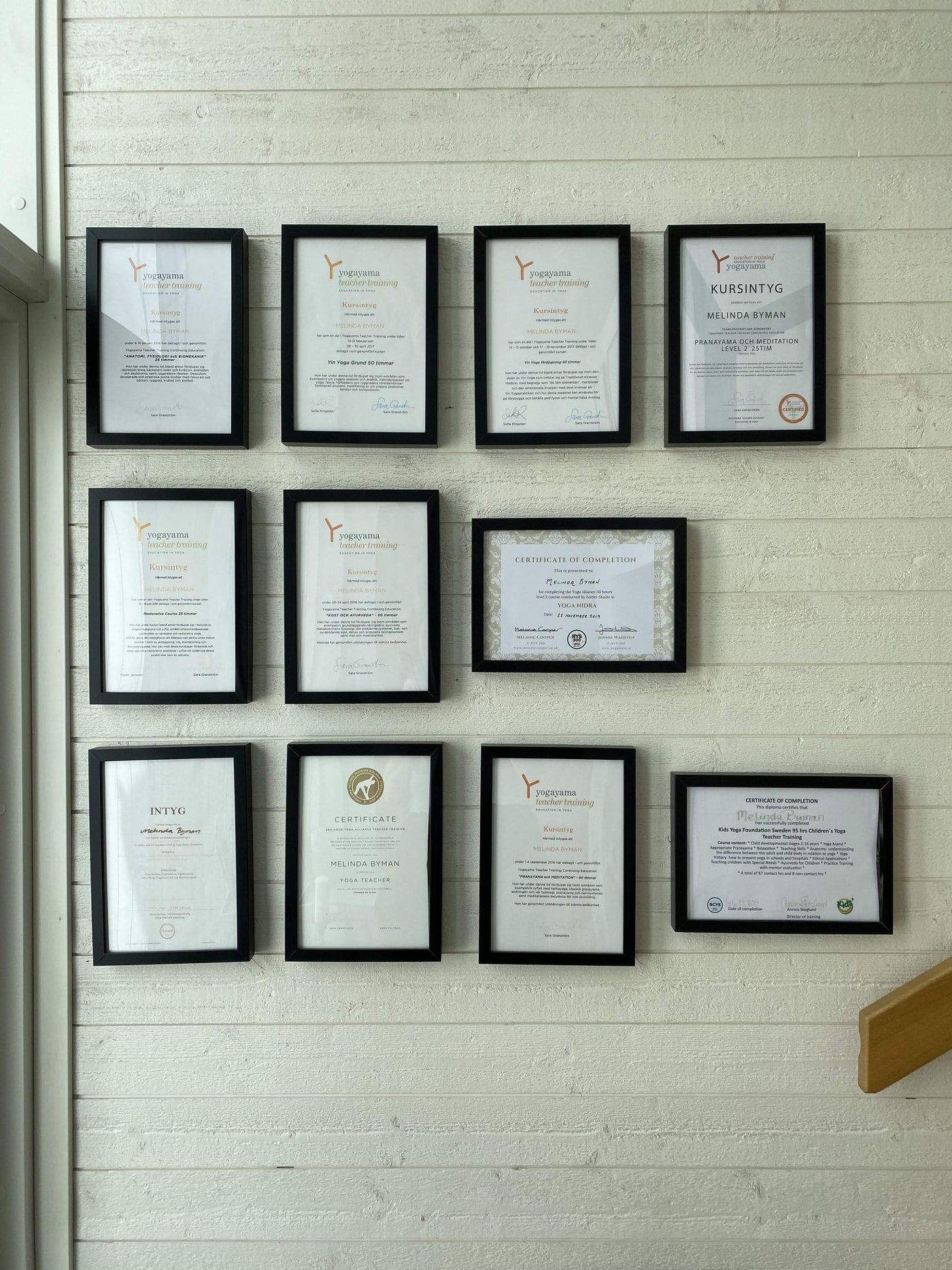 Tavelvägg med Melindas inramade certifikat från yogautbildningarna.