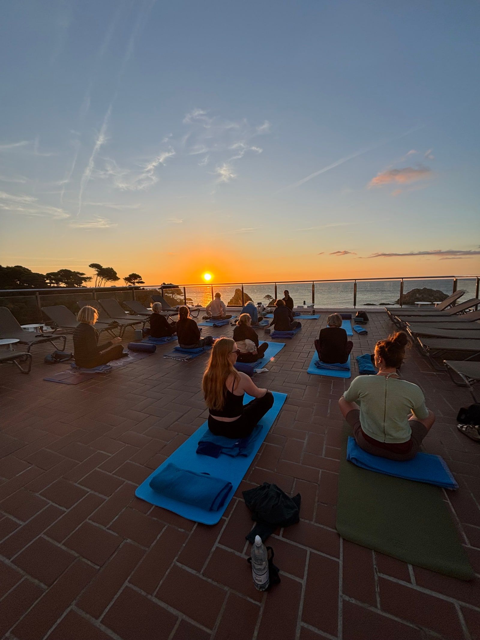 Sittande meditation på terrassen med solen som går upp över havet.