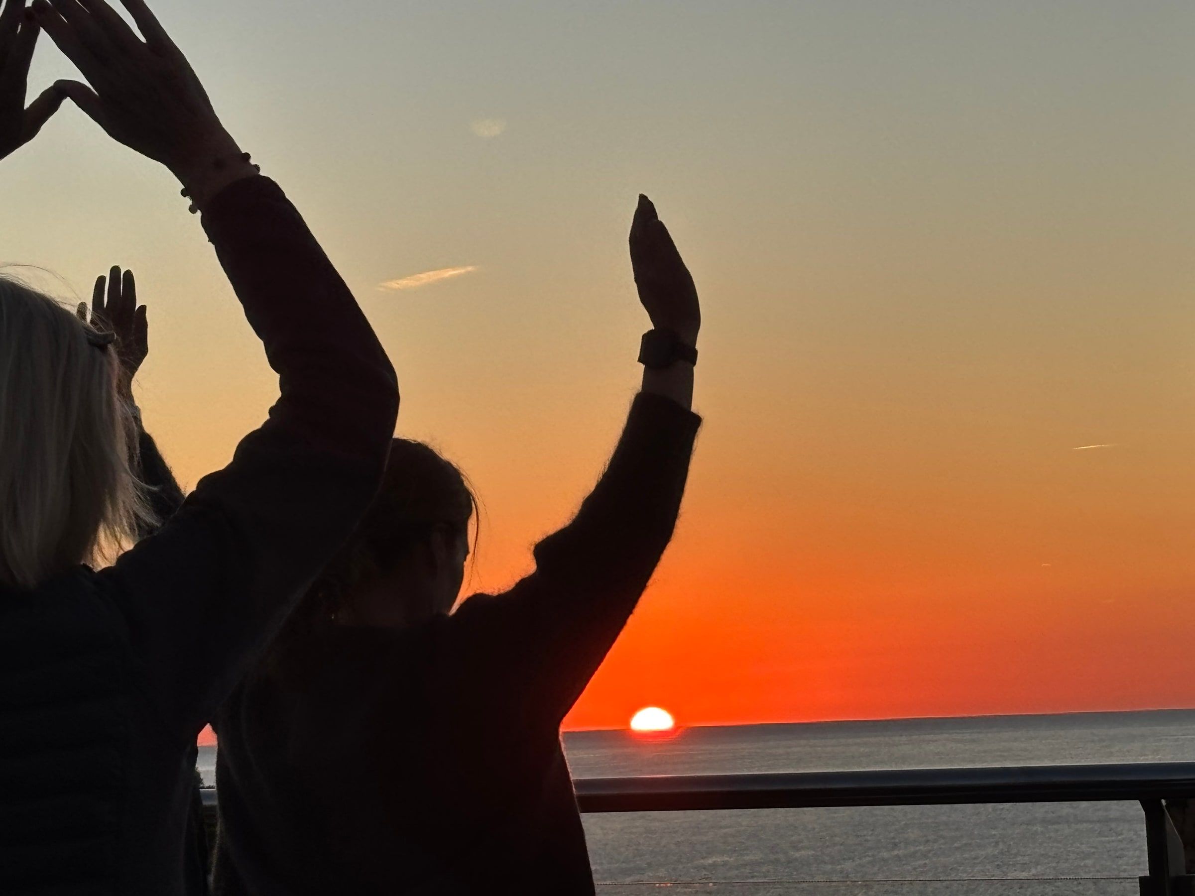 Armar i silhuett mot en orange solnedgång över havet i Tossa de Mar.