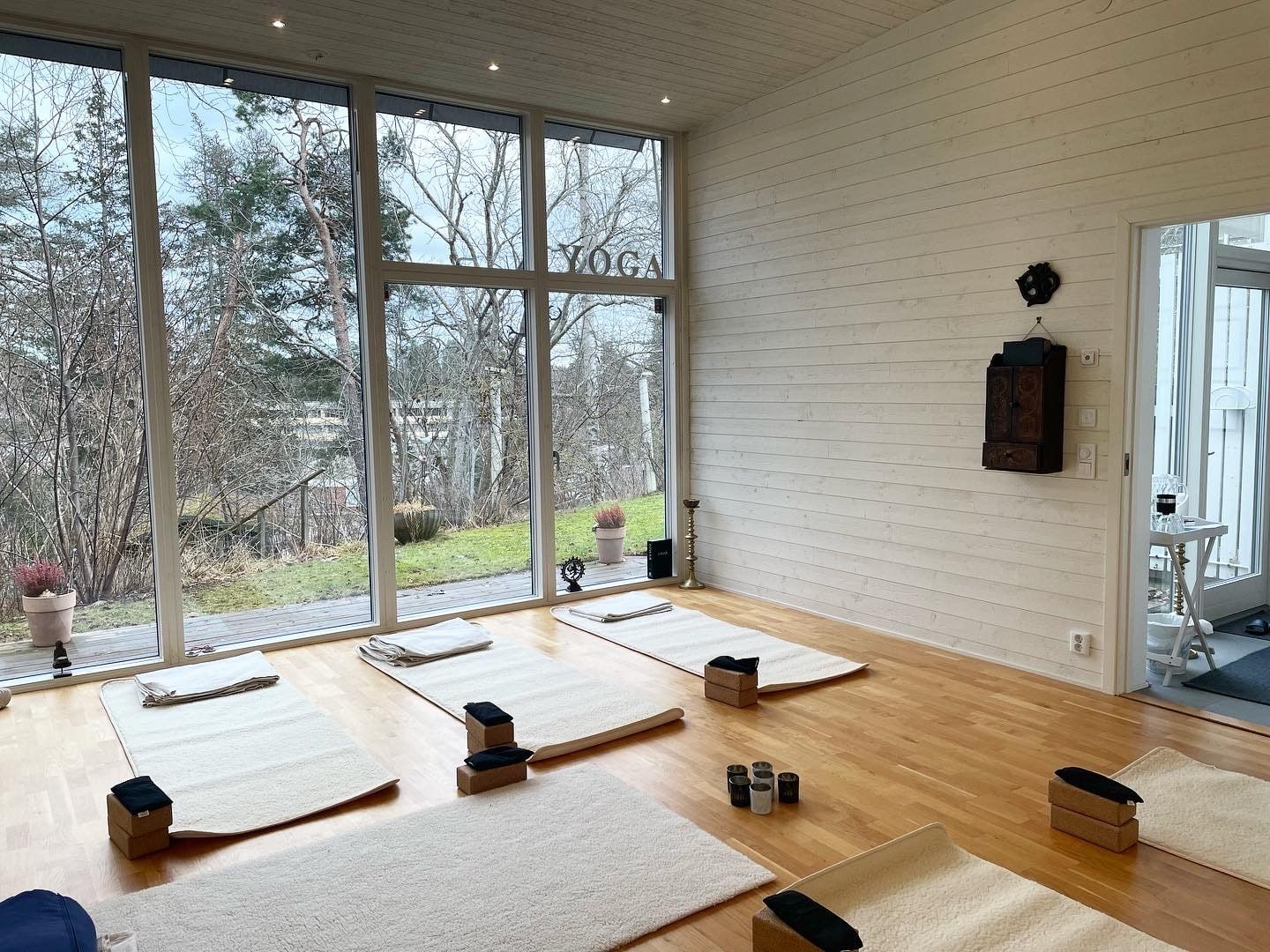 Yogasalen en vinterdag med ljusa mattor och ordet YOGA på glasväggen mot trädgården.
